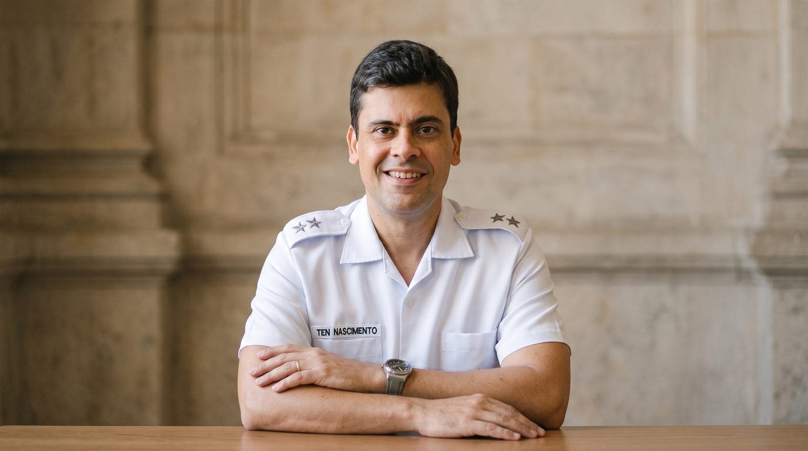 Dr. Marcus Felipe sorrindo, sentado à mesa, de uniforme branco do Exército Brasileiro.